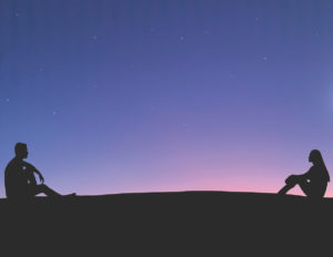 Two people sitting in silhouette against a dark sky